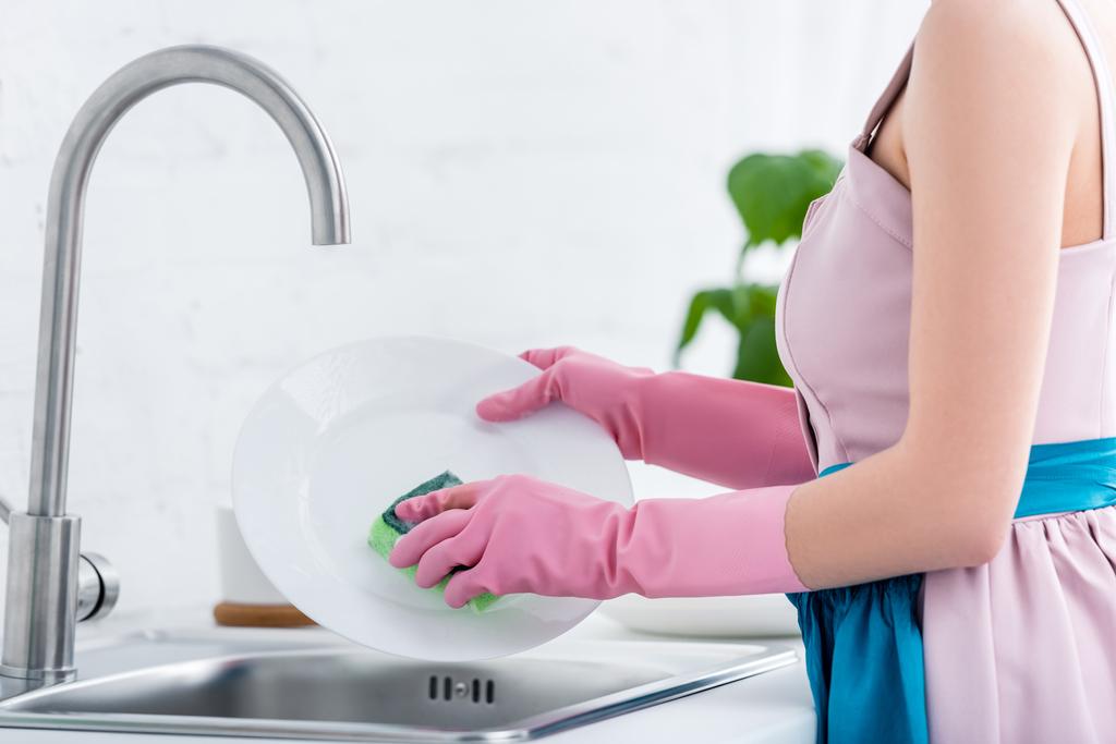 обрізаний вид молодої жінки в рожевих гумових рукавичках миття посуду на кухні
 - Фото, зображення