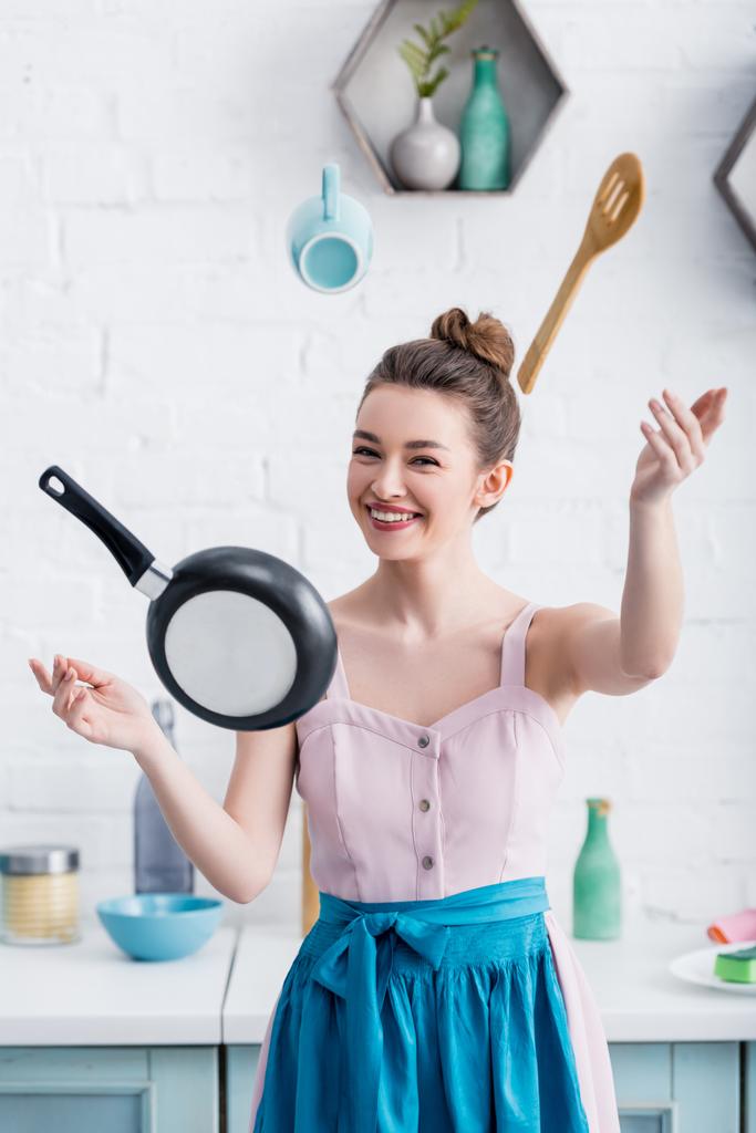 gülümseyen mutlu genç kadın havada uçan kaplar pişirme sırasında kameraya bakıyor  - Fotoğraf, Görsel