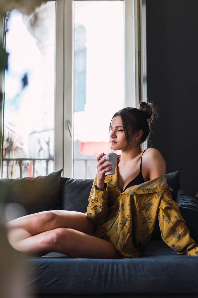 Очаровательная молодая женщина с чашкой сидя на диване
 - Фото, изображение