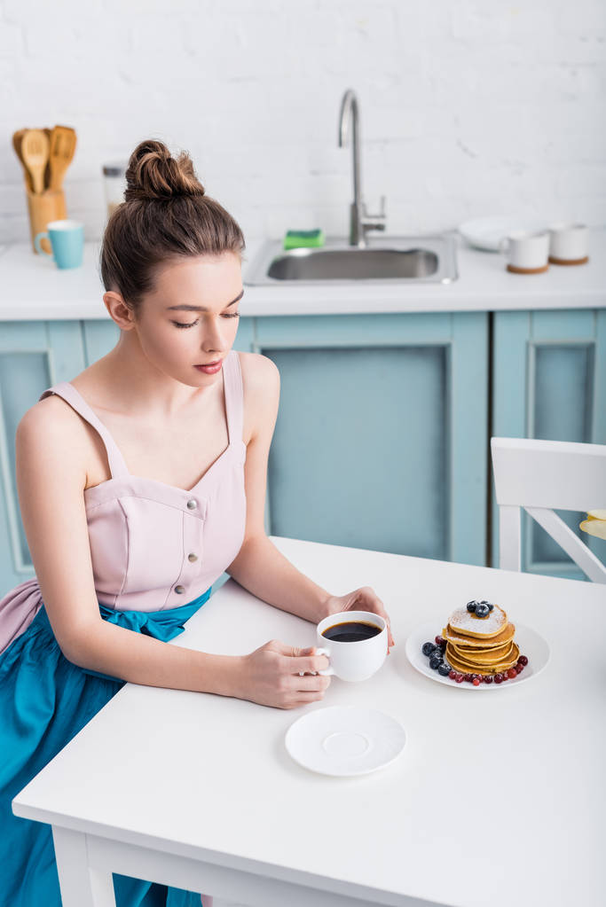 attraktive, elegante junge Frau sitzt am Tisch und trinkt Kaffee - Foto, Bild