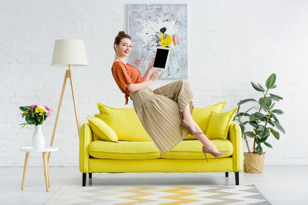 élégante jeune femme heureuse lévitant dans l'air et montrant tablette numérique avec écran blanc dans le salon
 - Photo, image