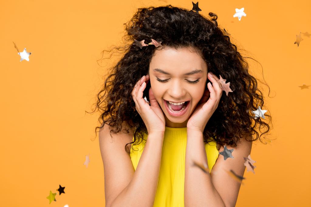 happy curly african american girl screaming near shiny confetti stars on orange  - Photo, Image