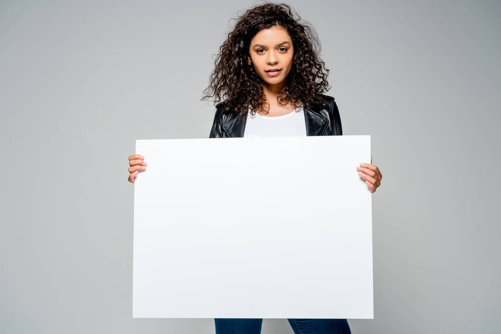 красива кучерява афроамериканська дівчина тримає порожній плакат, стоячи ізольовано на сірому
 - Фото, зображення