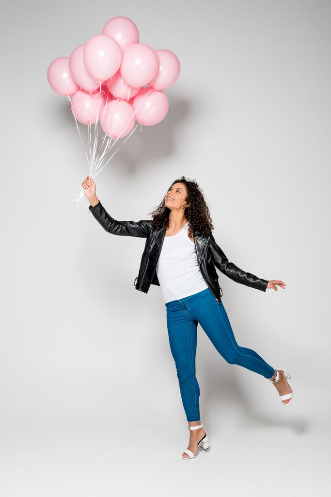 alegre afroamericana joven mujer sosteniendo rosa globos de aire en gris
 - Foto, Imagen