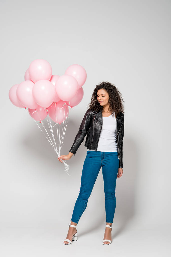 灰色の上にピンクの空気風船を持っている美しいアフリカ系アメリカ人の若い女性 - 写真・画像
