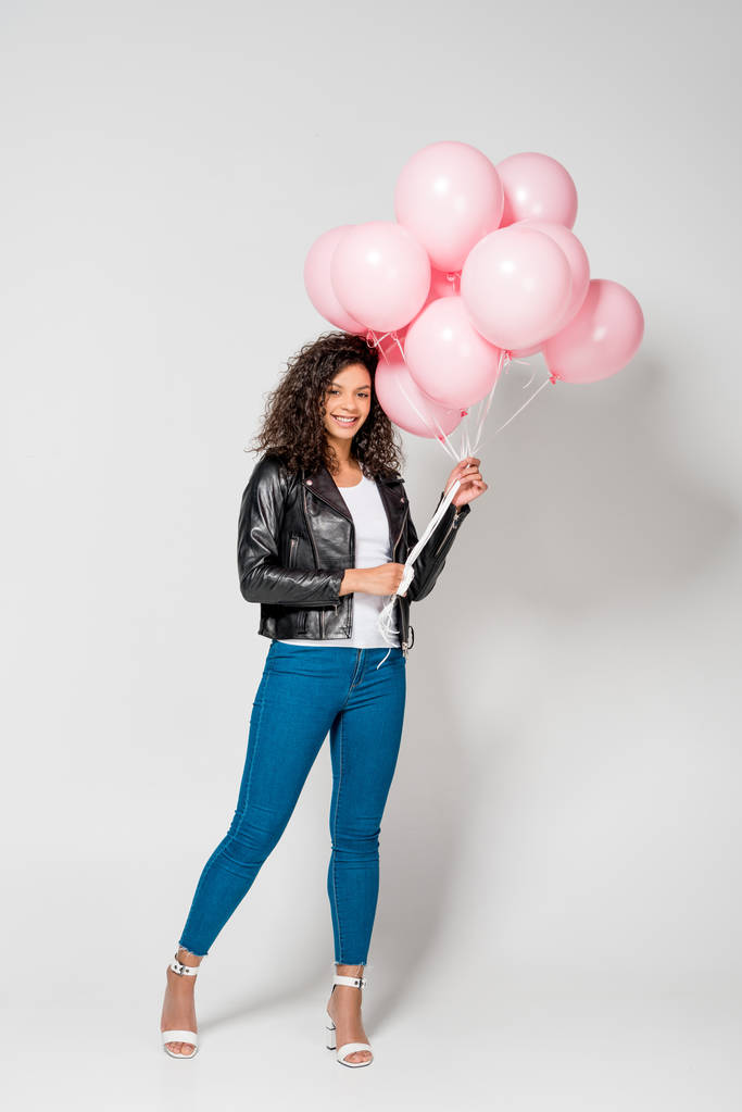 smiling african american young woman holding pink air balloons on grey - Photo, Image