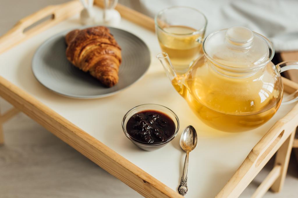 selectieve focus van houten tray met croissant, jam, thee en theepot - Foto, afbeelding