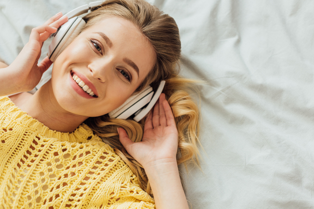 ylhäältä kaunis hymyilevä nuori nainen kuulokkeet makaa sängyssä, katsot kameraa ja kuunnella musiikkia
 - Valokuva, kuva
