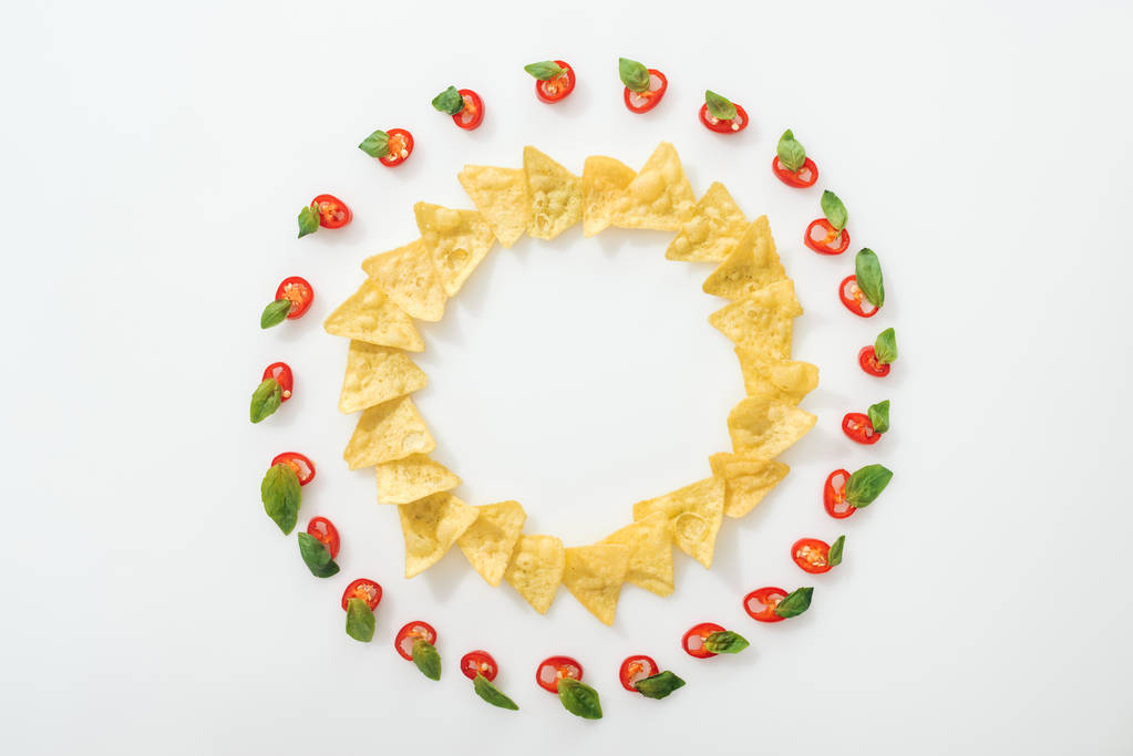 bovenaanzicht van gesneden chilipepers en smakelijke nachos met basilicum blaadjes op witte achtergrond  - Foto, afbeelding