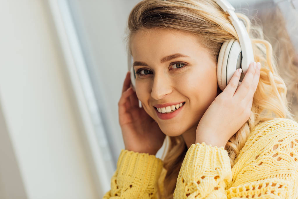 красива усміхнена молода жінка в навушниках дивиться на камеру, слухаючи музику вдома
 - Фото, зображення