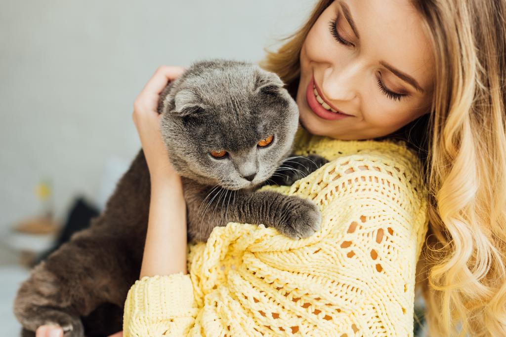 επιλεκτική εστίαση του όμορφη χαμογελαστή κορίτσι αγκαλιάζει χαριτωμένο σκωτσέζικη Δίπλωση γάτα  - Φωτογραφία, εικόνα