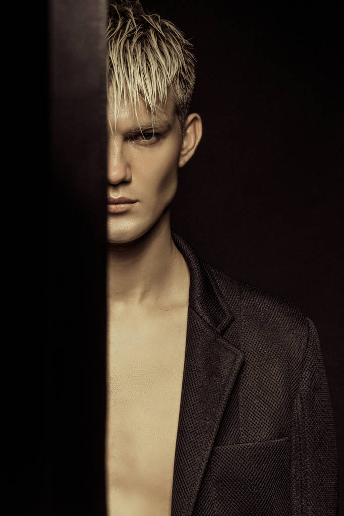 hübsche entblößte blonde männliche Modell trägt schwarzen Anzug auf schwarzen isolierten Schrift Hintergrund - Foto, Bild