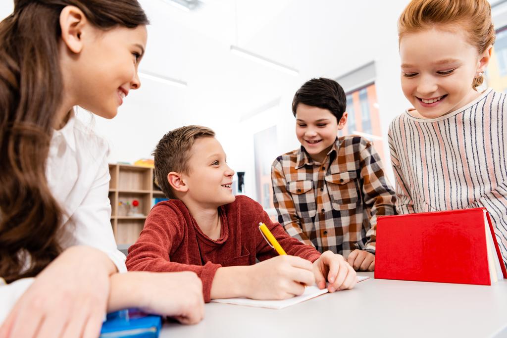 Lächelnde Schüler mit Notizbüchern und Büchern diskutieren im Klassenzimmer - Foto, Bild