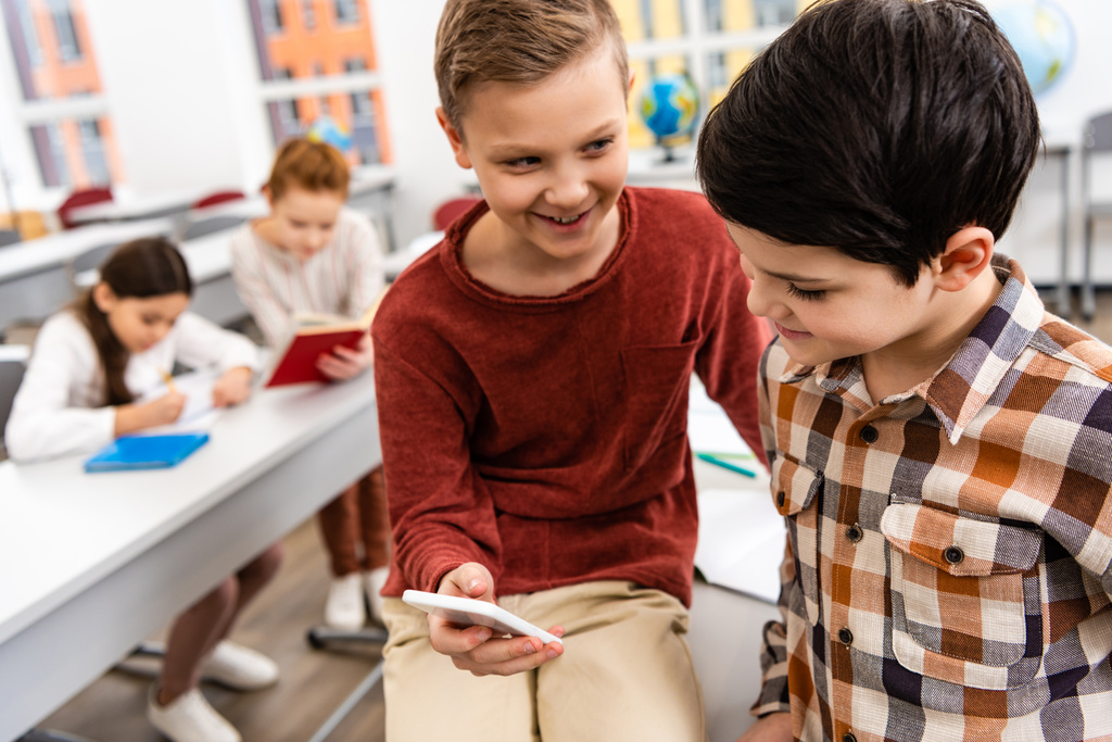 zwei lächelnde Schüler mit Smartphone im Klassenzimmer während der Bremse - Foto, Bild
