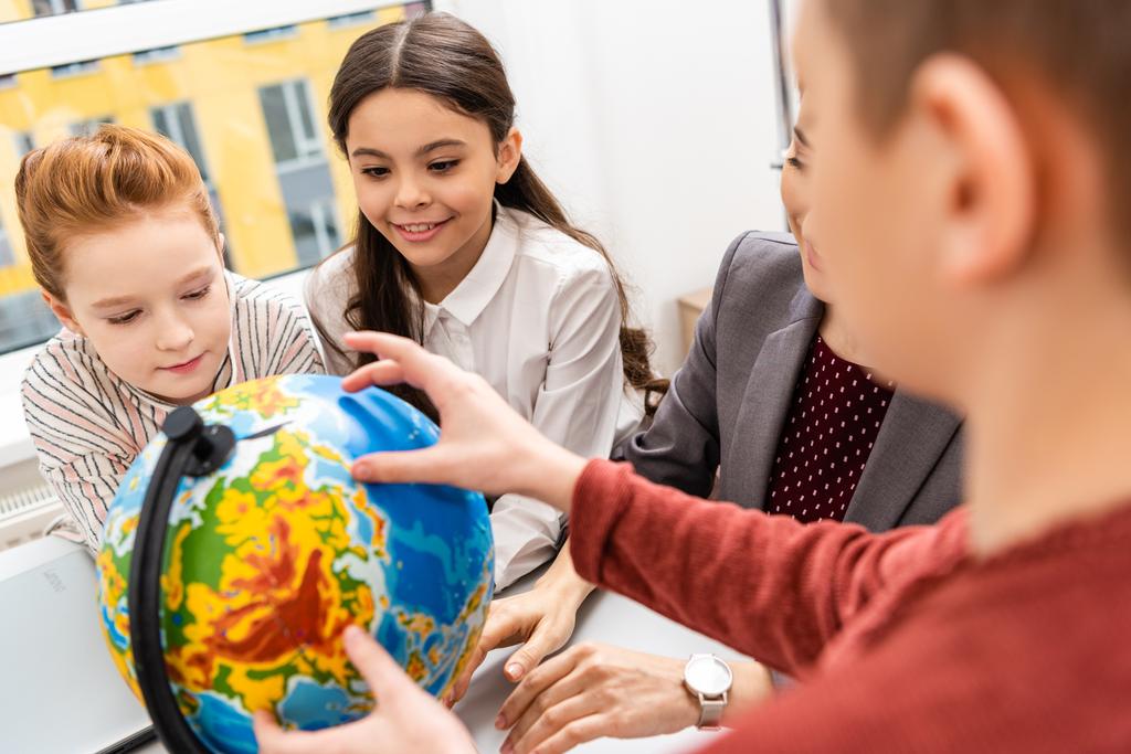 Обрезанный вид учеников и учителей, смотрящих на земной шар во время изучения географии в классе
 - Фото, изображение