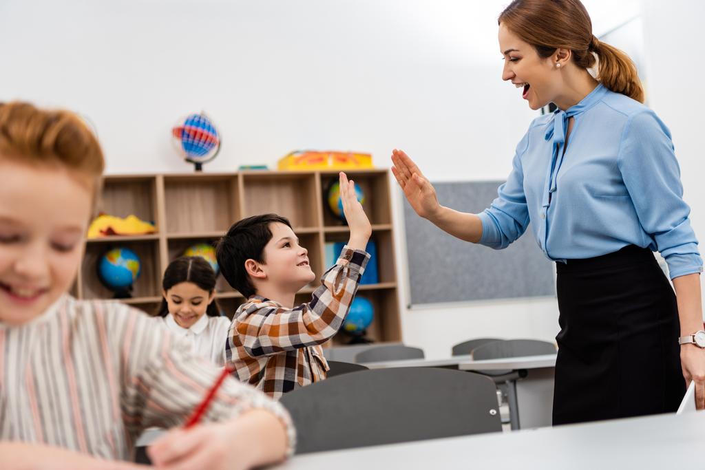 Smiling teacher and pupil raising hands for high five in classroom - Photo, Image