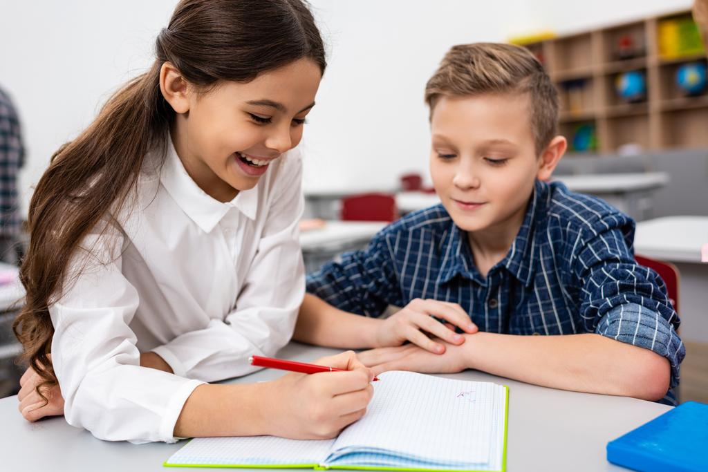 Два ученика пишут в блокноте за столом в классе
 - Фото, изображение
