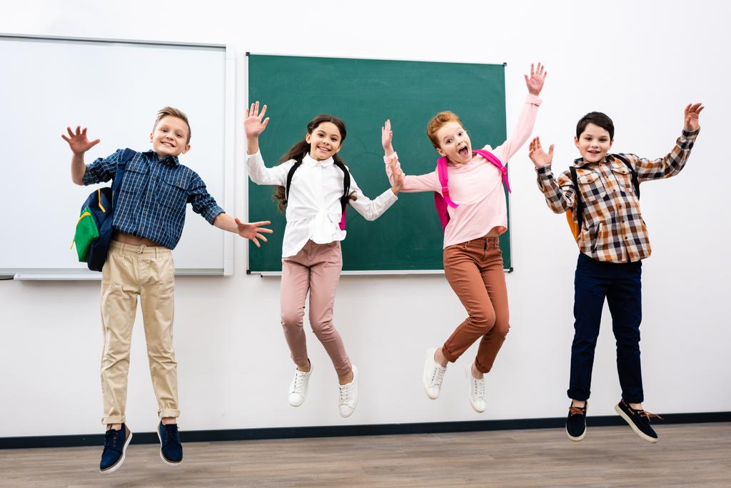 Čtyři žáci s batohy skáčou před tabuli - Fotografie, Obrázek