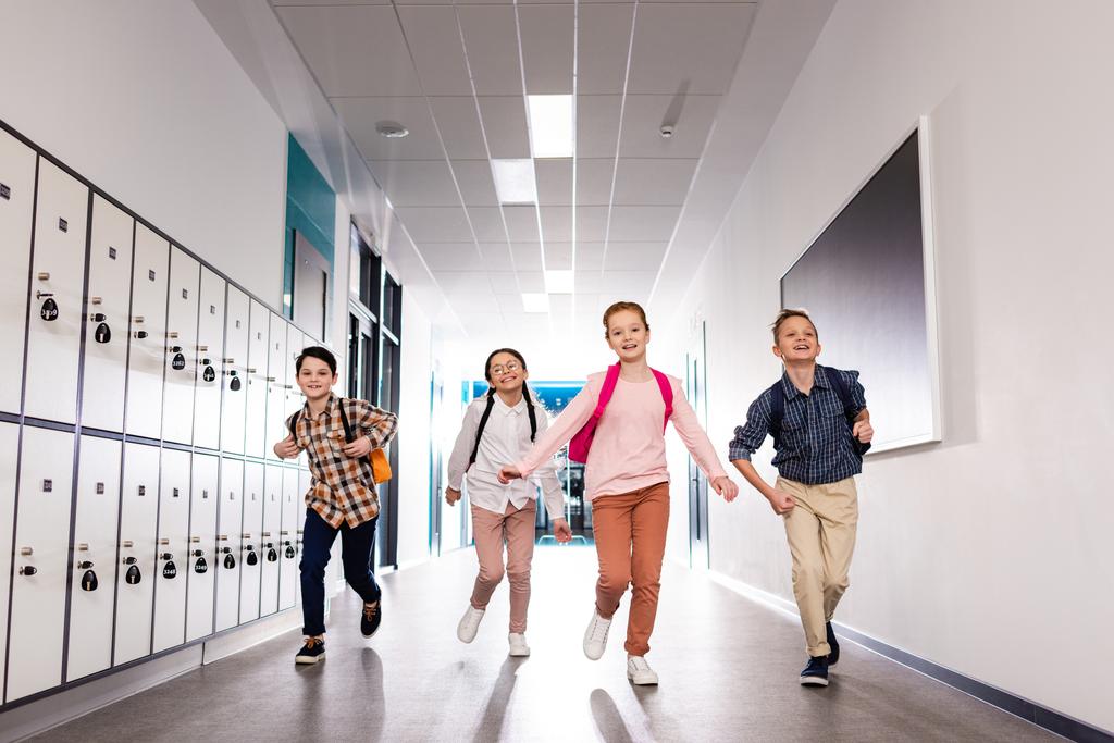 Quatro alunos animados com mochilas correndo corredor depois das aulas
 - Foto, Imagem