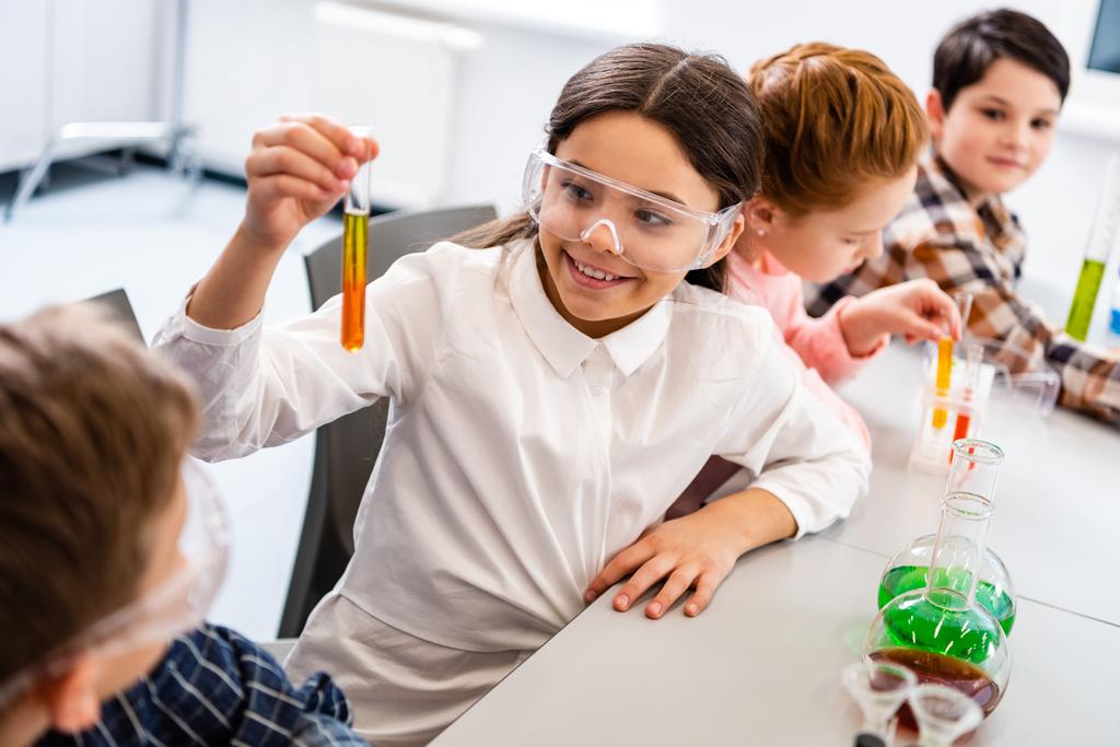 Ученики в защитных очках держат фляжки во время урока химии
 - Фото, изображение