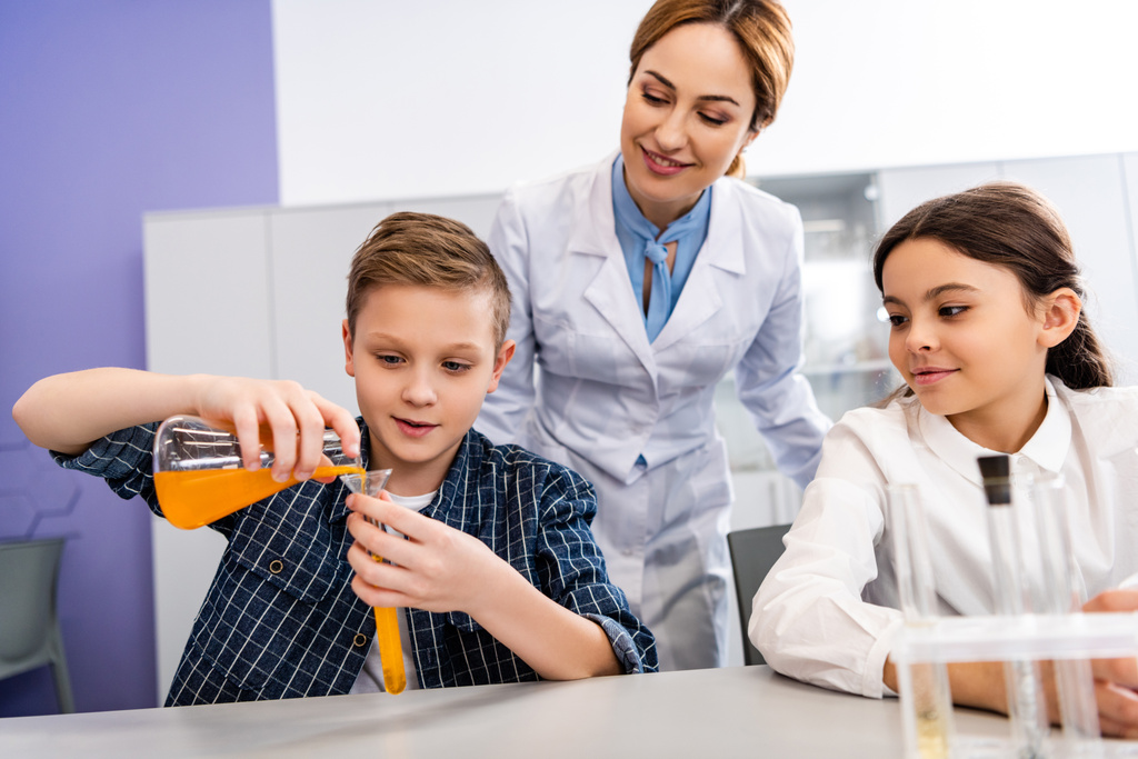 Chemistry teacher looking at pupil with beaker and flask in classroom - Photo, Image