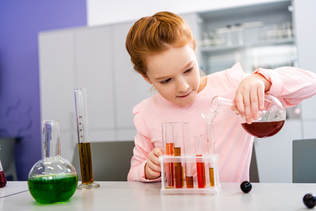 Mosolygó iskoláslány gazdaság főzőpohár és csinálás kémiai kísérlet közben kémia lecke  - Fotó, kép