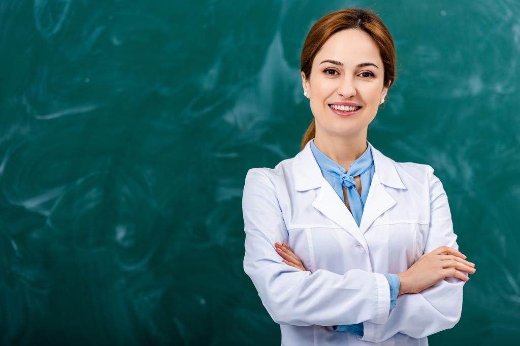 Professeur de chimie souriant en manteau blanc debout avec les bras croisés devant le tableau noir
 - Photo, image