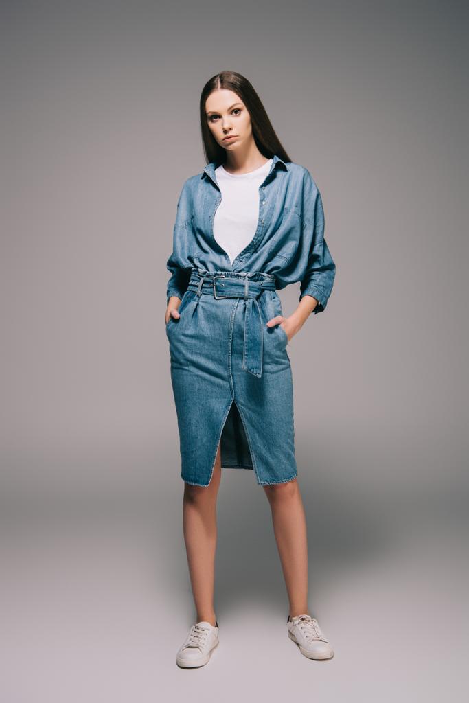 young adult and beautiful woman in denim dress with hands in pockets looking at camera - Photo, Image