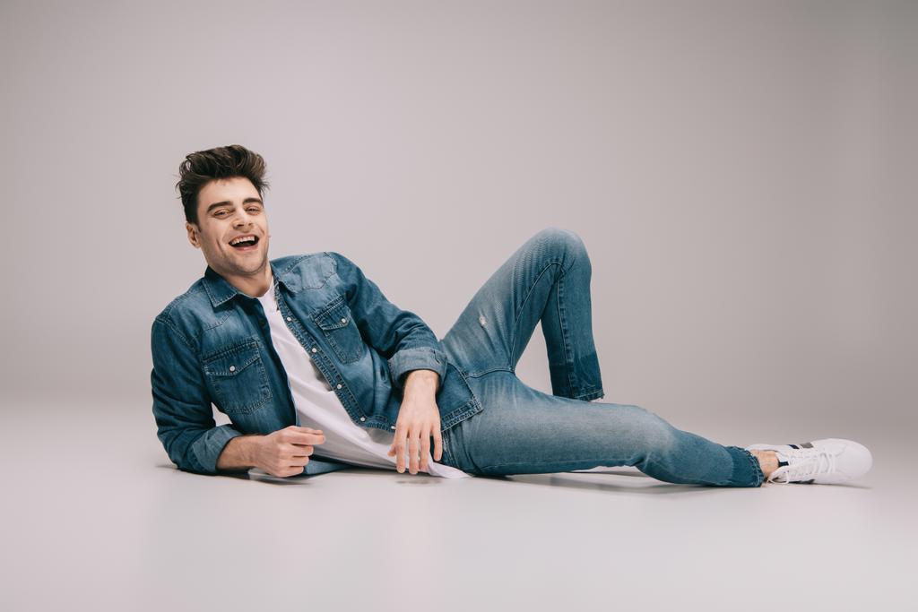 hombre sonriente y guapo en jeans, falda y camiseta acostado en el suelo y mirando a la cámara
 - Foto, Imagen