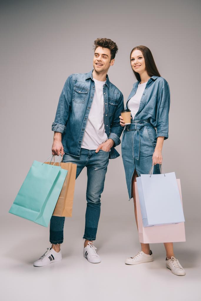 Dziewczyna w Jeansowa sukienka trzyma kubek papierowy i przystojny chłopak w dżinsy i koszulę, trzymając torby na zakupy - Zdjęcie, obraz