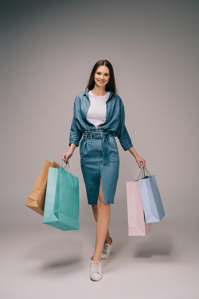 mujer sonriente y hermosa en vestido de mezclilla sosteniendo bolsas de compras y mirando a la cámara
 - Foto, imagen
