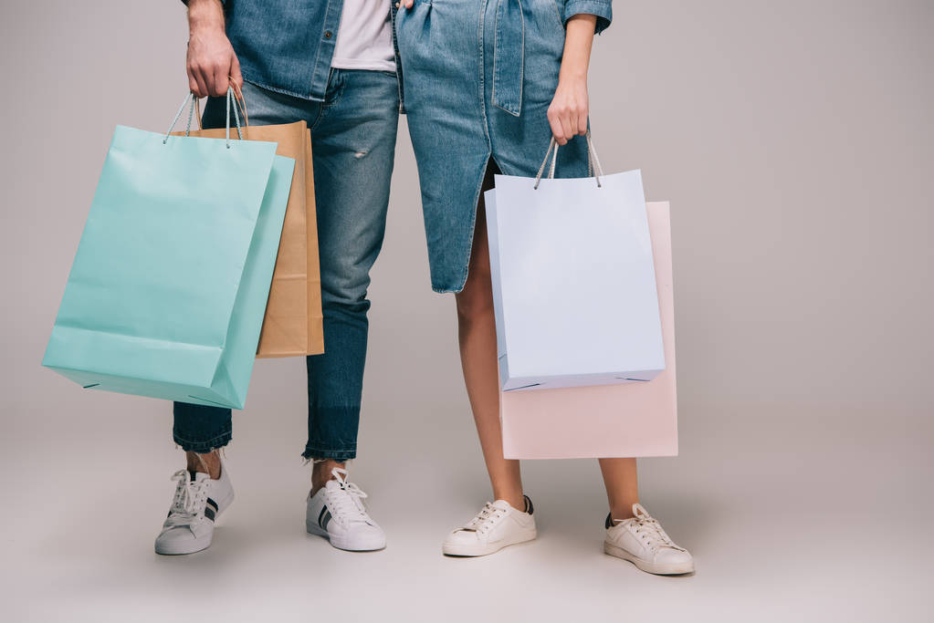 vista cortada de homem e mulher segurando sacos de compras em fundo cinza
  - Foto, Imagem