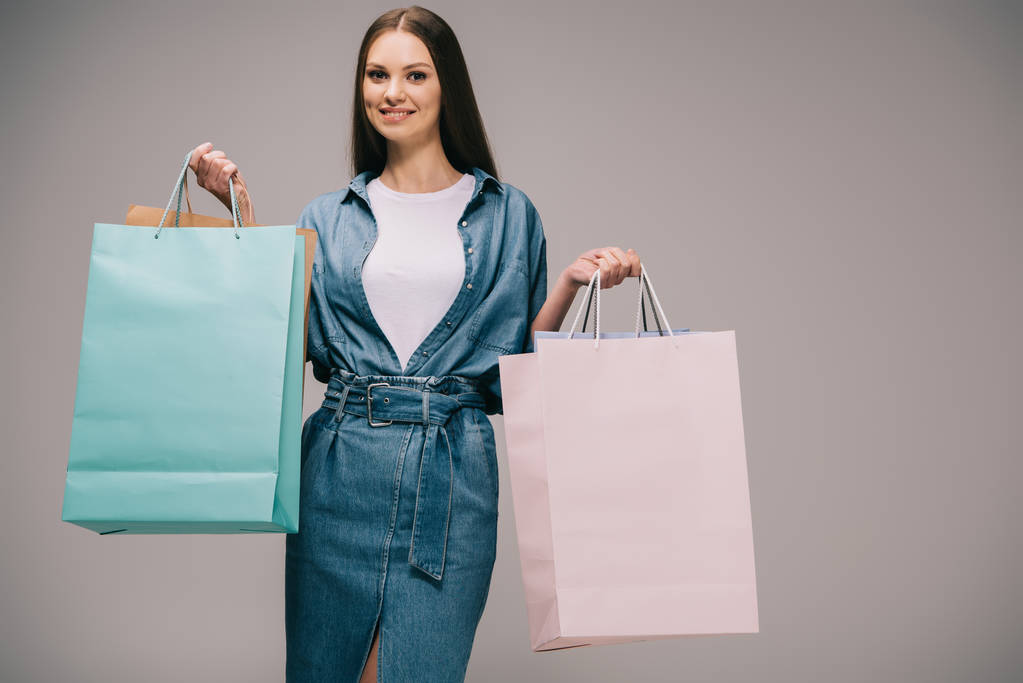 улыбающаяся и красивая женщина в джинсовом платье, держащая сумки с покупками и смотрящая в камеру
 - Фото, изображение