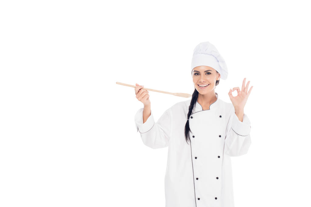Uśmiechnięty kucharz w jednolite gospodarstwa drewnianej szpatułki i Wyświetlono porządku znak na białym tle - Zdjęcie, obraz