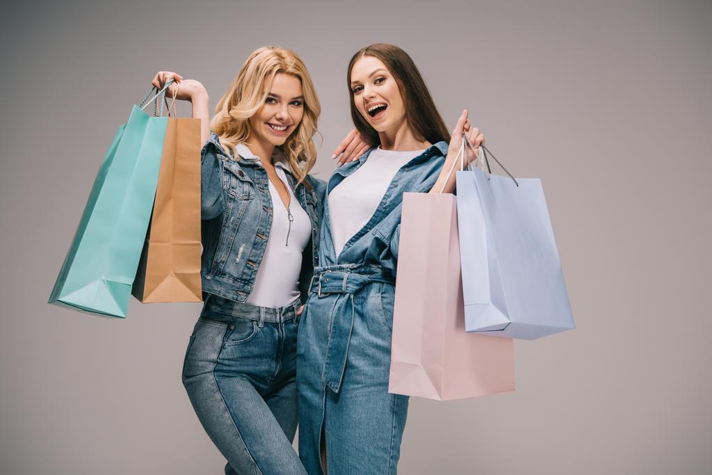 beautiful blonde and happy brunette women in denim clothes holding shopping bags and smiling   - Photo, Image