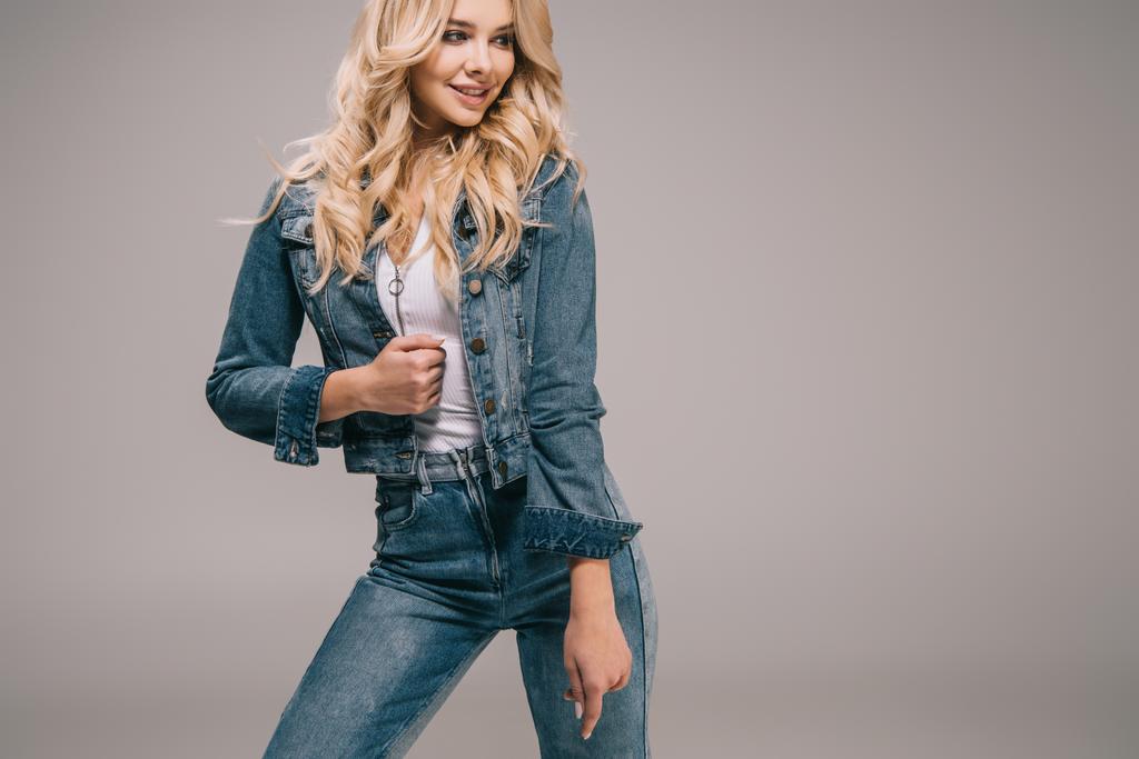 attraente donna bionda in giacca di jeans e jeans sorridente e guardando altrove
  - Foto, immagini