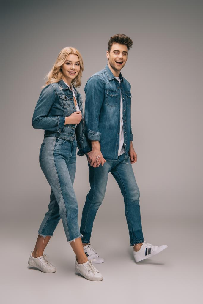 smiling boyfriend and attractive girlfriend in denim clothes holding hands and looking at camera  - Photo, Image
