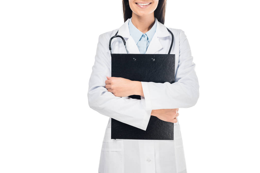 Częściowy widok uśmiechający się lekarz w białym płaszczu przytrzymanie Schowka na białym tle - Zdjęcie, obraz