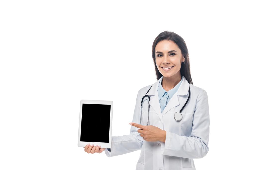 Médico sonriente con estetoscopio apuntando con el dedo a la tableta digital con pantalla en blanco aislado en blanco
 - Foto, Imagen