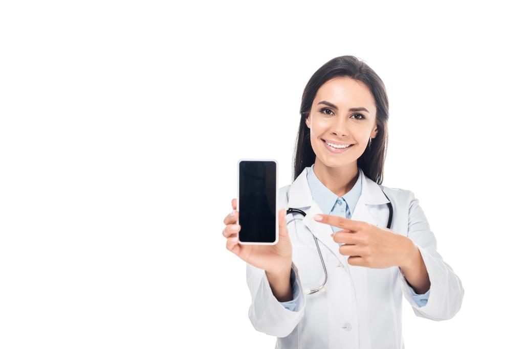 Doctor in white coat with stethoscope pointing with finger at smartphone with blank screen isolated on white - Photo, Image