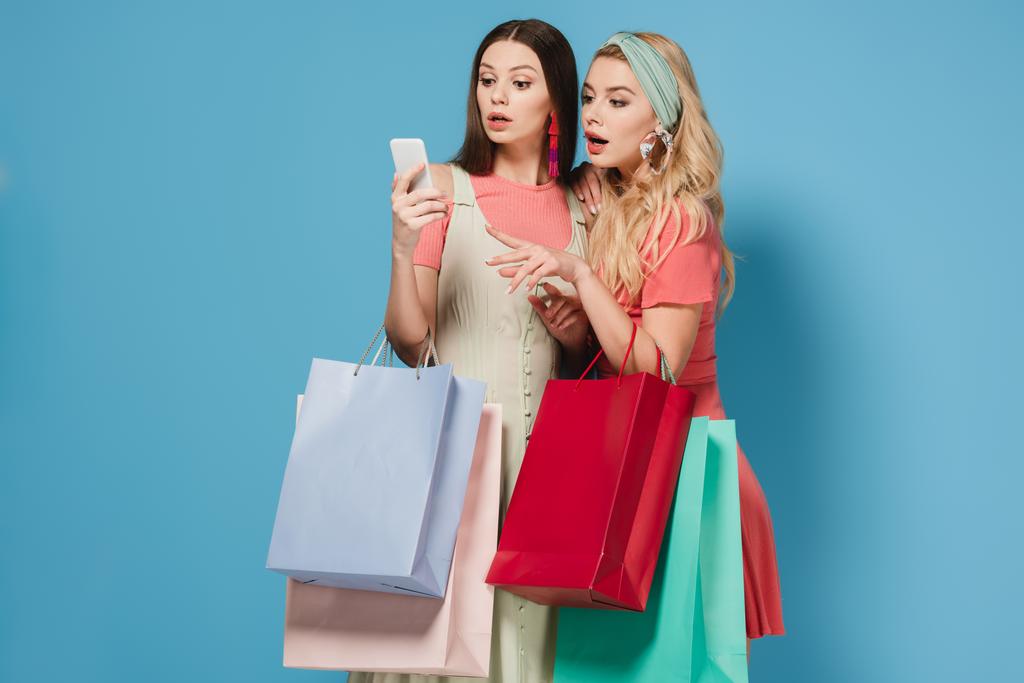 surprise brune et les femmes blondes en robes tenant des sacs à provisions et en utilisant un smartphone
  - Photo, image