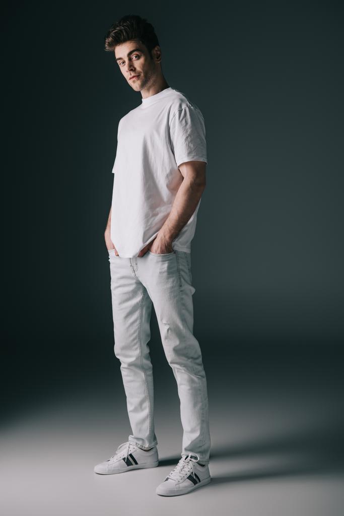 hombre guapo en camiseta blanca y jeans con las manos en los bolsillos mirando a la cámara
  - Foto, imagen