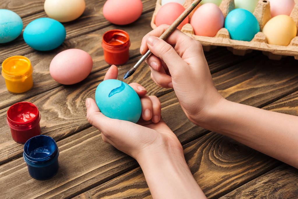 cropped view of woman decorating easter eggs with paintbrush at wooden table - Photo, Image