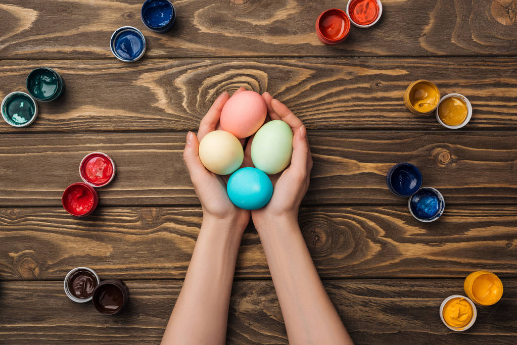 верхний вид женщины, держащей пасхальные яйца на деревянной поверхности красками
 - Фото, изображение
