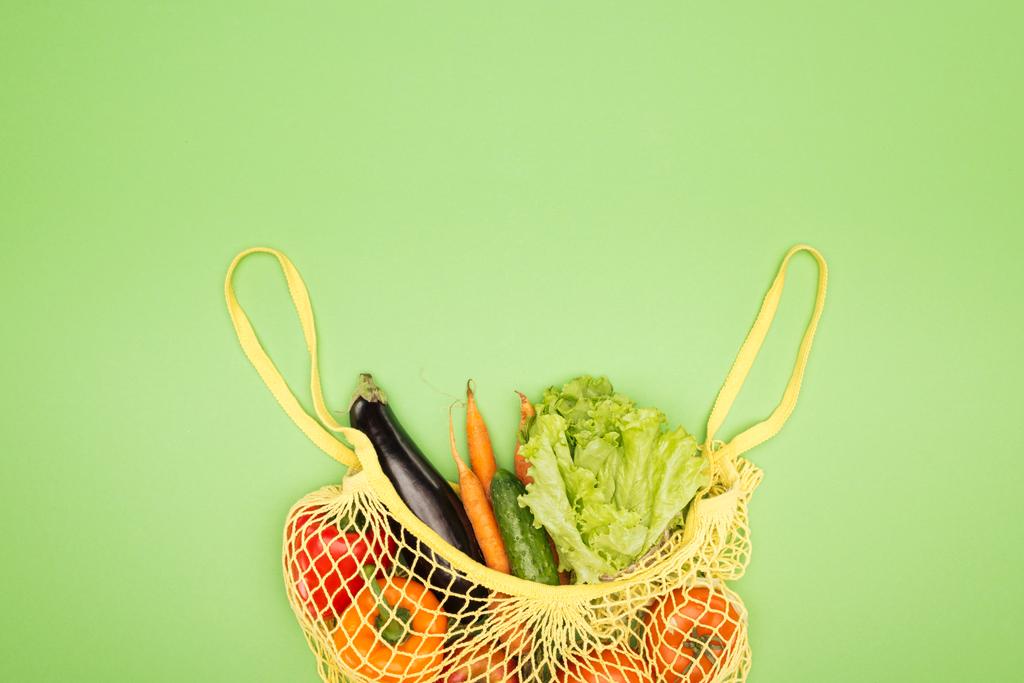 top view of yellow string bag with organic vegetables on light green surface with copy space - Photo, Image