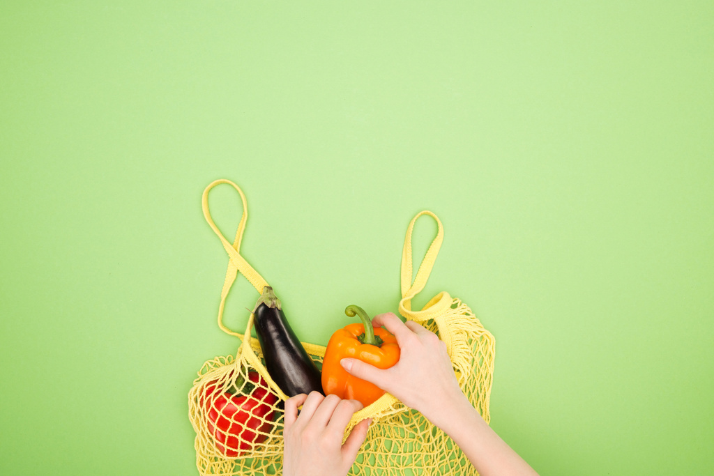 vue partielle de la femme prenant du poivron frais dans un sac à ficelle jaune avec des légumes entiers sur une surface vert clair
 - Photo, image