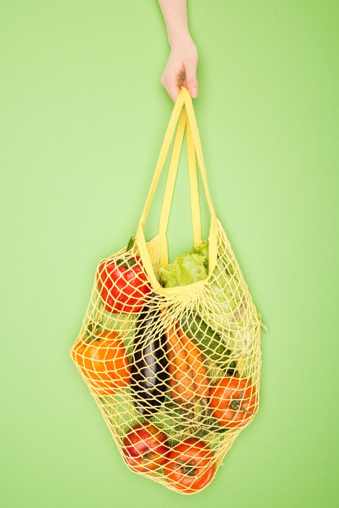 partial view of woman holding string bag with vegetables on light green  - Photo, Image