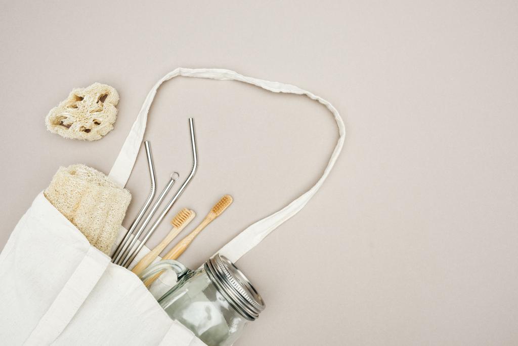 escovas de dentes de bambu, loofah orgânico, jarra e palhas de aço inoxidável em saco de algodão branco em fundo cinza com espaço de cópia
 - Foto, Imagem