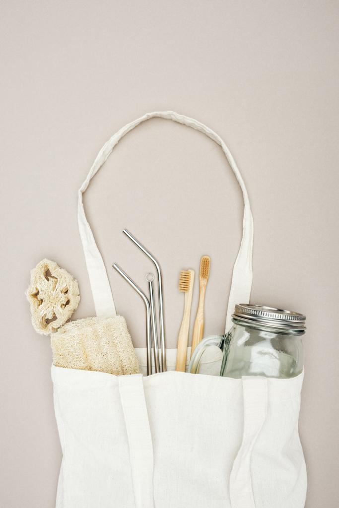 白い綿の袋の竹の歯ブラシ、有機ヘチマ、瓶およびステンレス鋼のわらは灰色の背景にある - 写真・画像