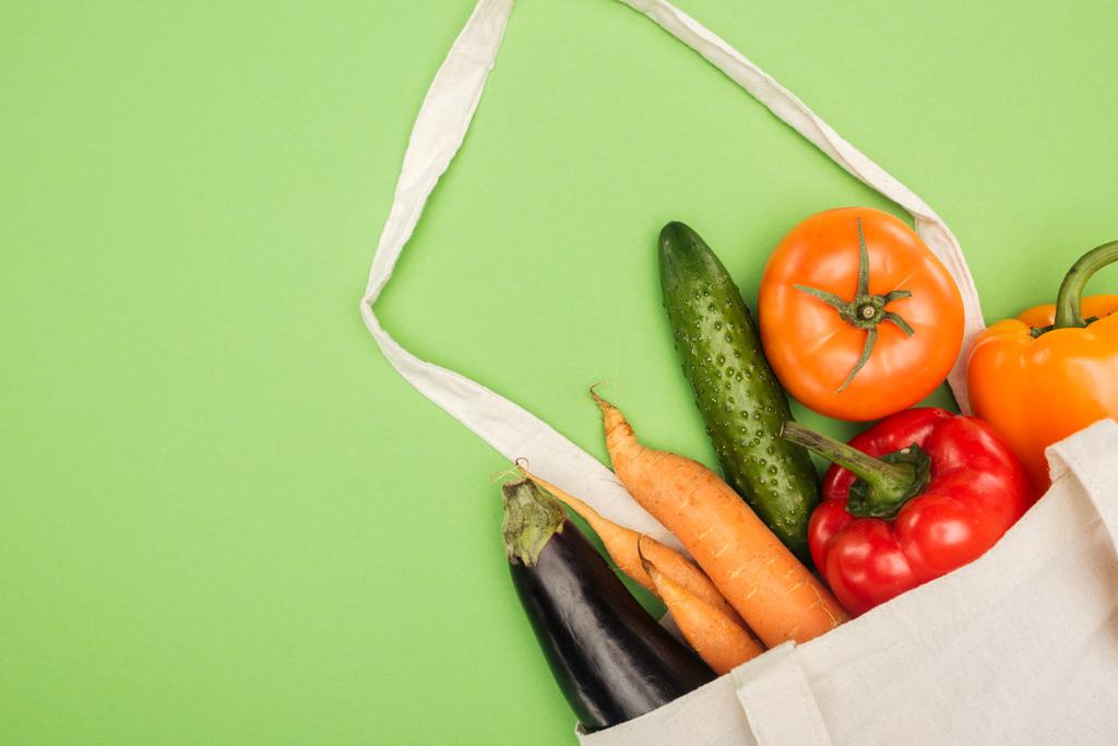 βαμβακερή σακούλα με φρέσκα ώριμα λαχανικά σε ανοιχτό πράσινο φόντο - Φωτογραφία, εικόνα